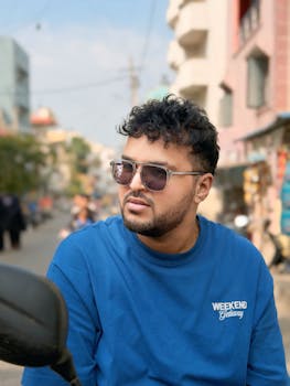 Casual portrait of a man wearing sunglasses and a blue shirt in an urban street setting.