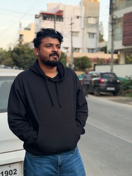 Casual portrait of a man in a hoodie standing on a quiet street with buildings in the background.