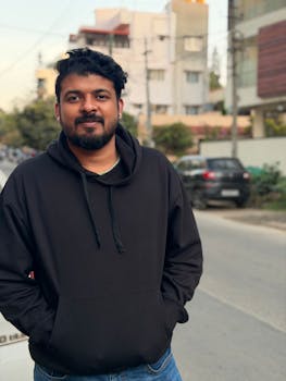 Man in black hoodie standing on a city street during daylight.