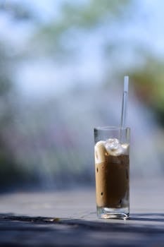 Tall glass of iced coffee with straw outside on a sunny day.