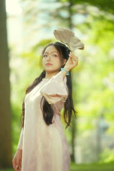 Elegant woman holding a fan in traditional clothing, set against a lush green background.