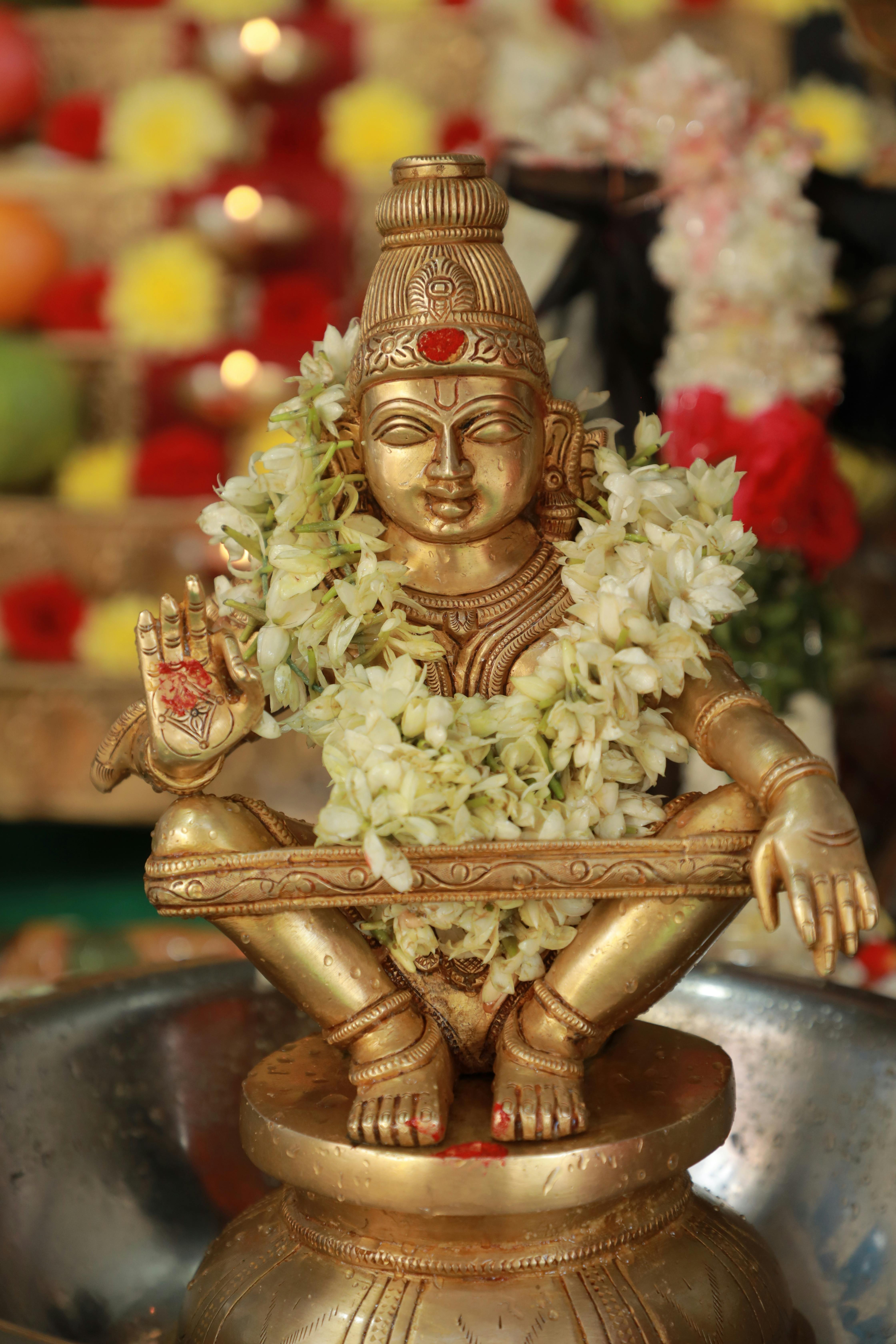 A golden Hindu deity statue adorned with a white floral garland, symbolizing peace.