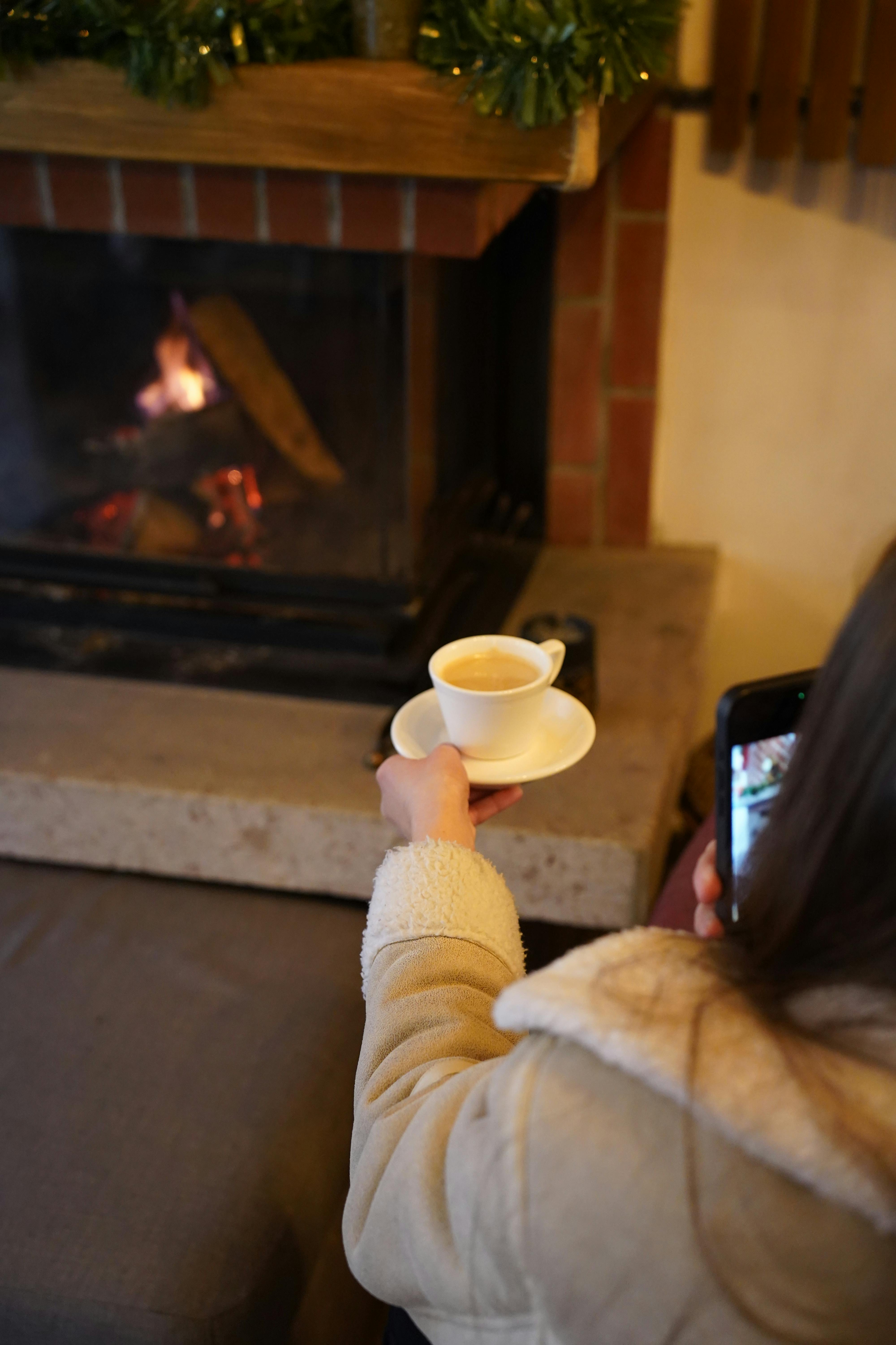 Enjoy a cozy winter scene by the fireplace with a coffee and smartphone in Çanakkale, Türkiye.