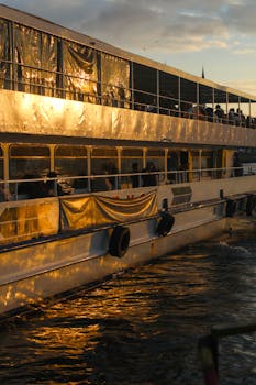A cruise ship's side reflecting golden sunlight at sunset, with passengers on deck.