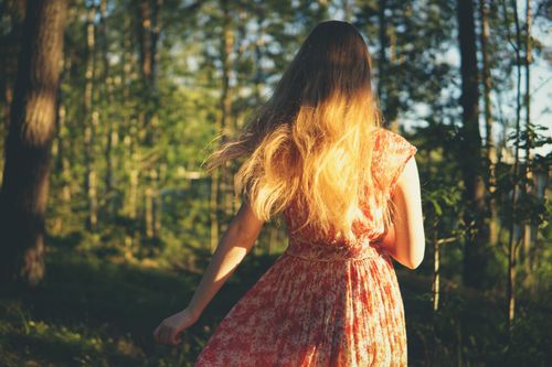 Free A woman in a floral dress walks through a sunlit forest. Bright back view. Stock Photo