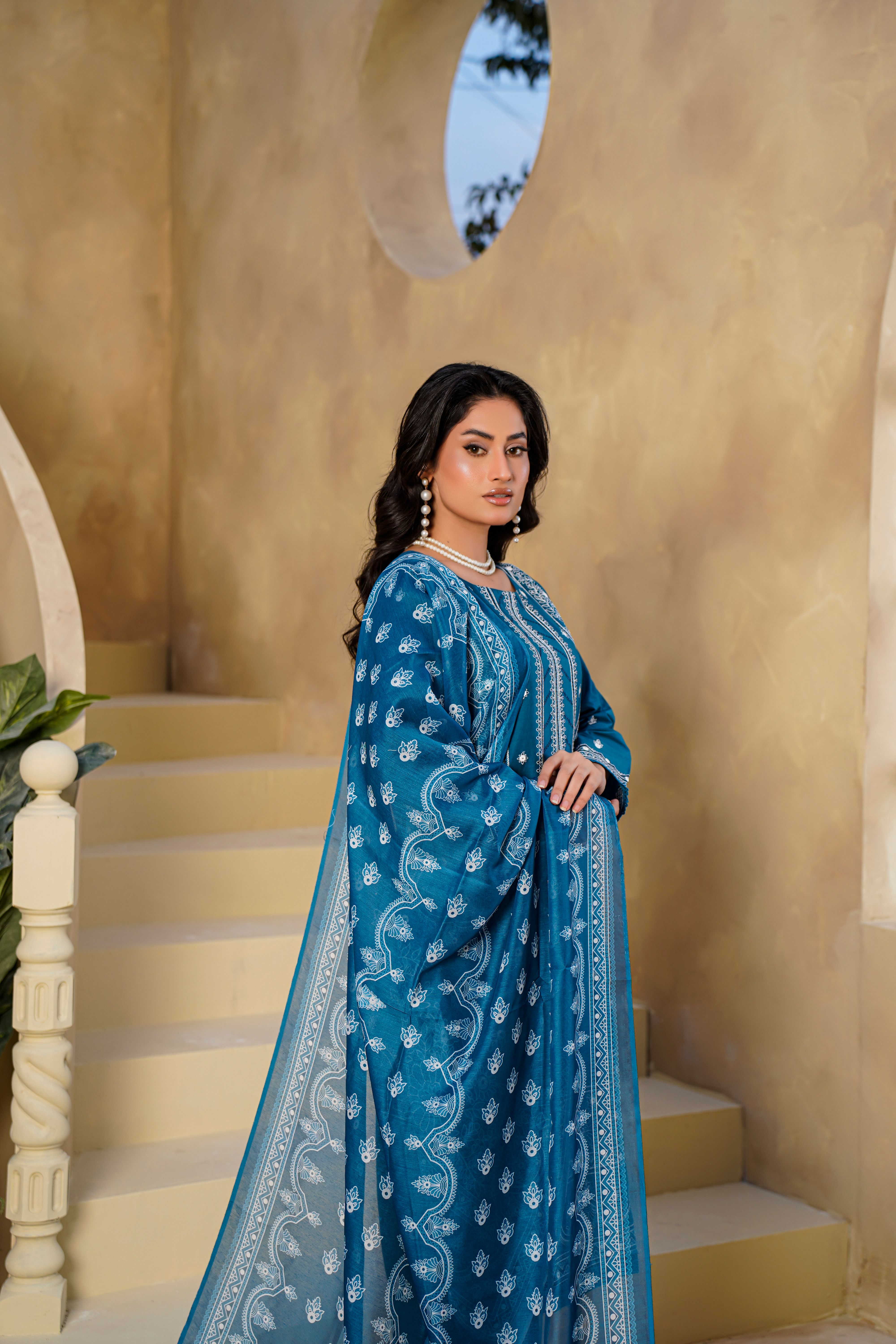 A woman in a traditional blue dress stands gracefully indoors, exuding elegance.