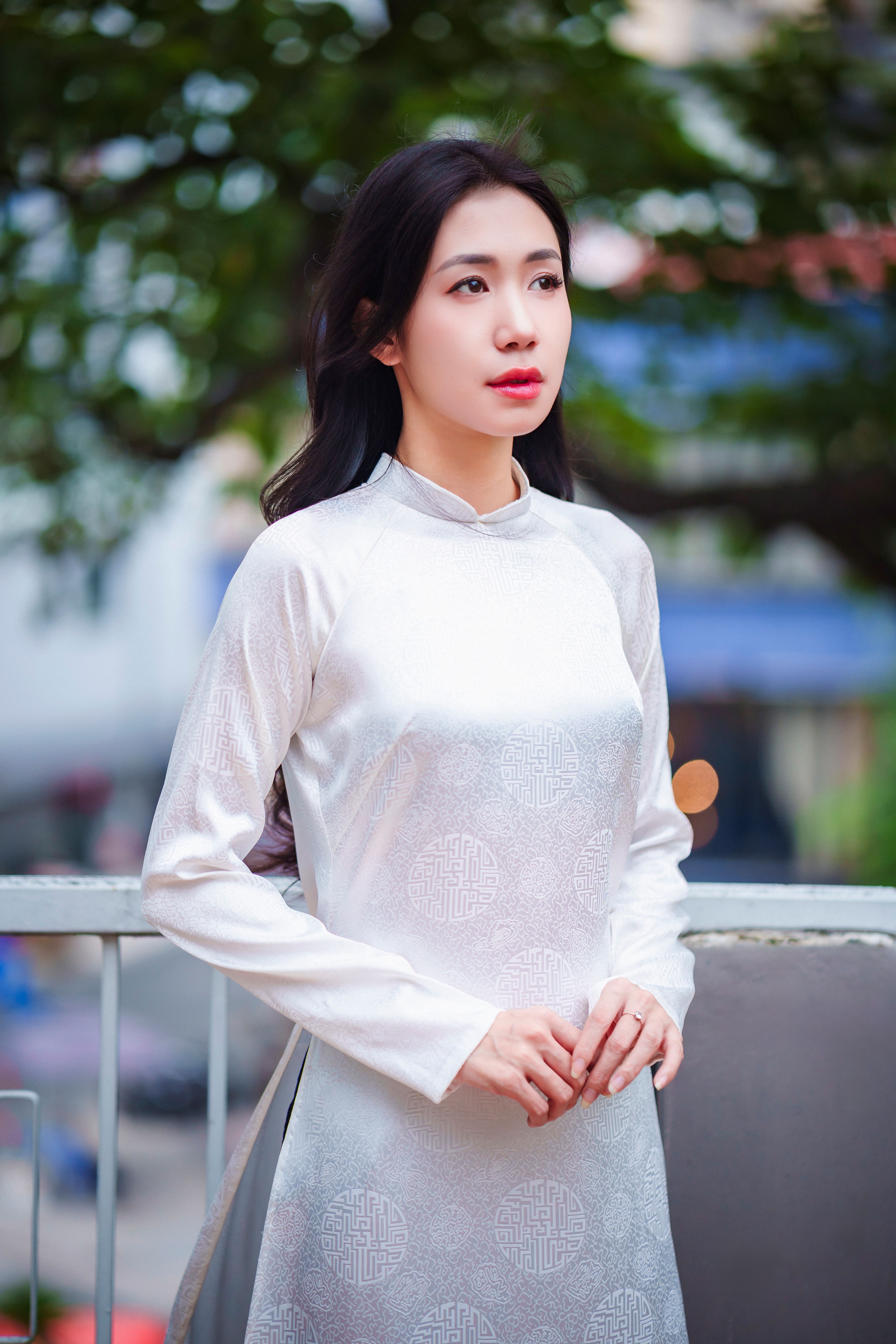 A woman in a traditional white áo dài stands elegantly outdoors in Ho Chi Minh City, capturing grace