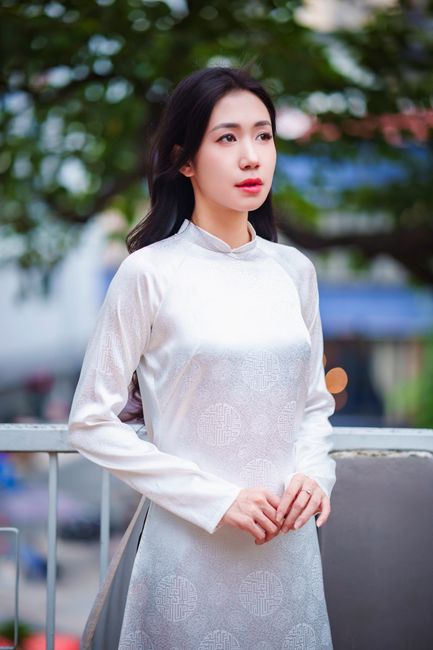 A woman in a traditional white áo dài stands elegantly outdoors in Ho Chi Minh City, capturing grace