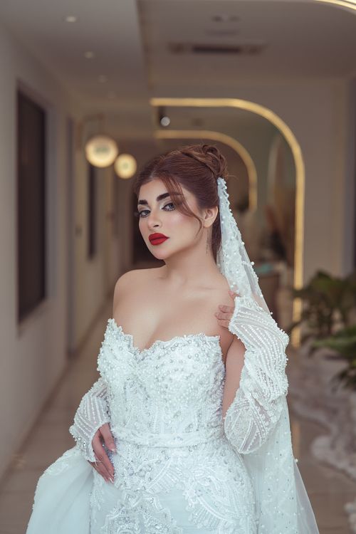 Free A stunning bride poses in an elegant lace wedding dress with intricate details indoors. Stock Photo