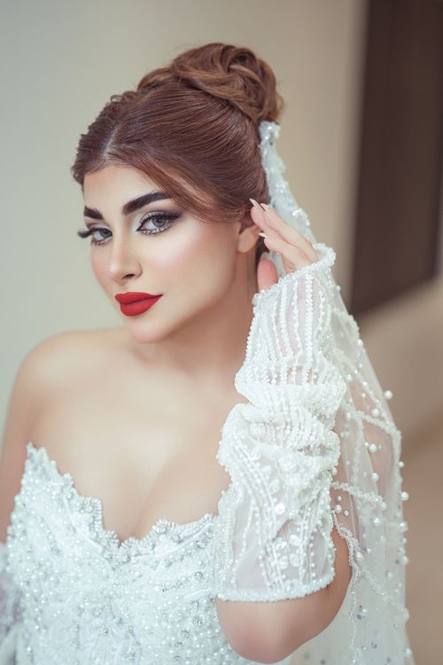 Free Beautiful bride in white gown with pearl details posing gracefully indoors. Stock Photo