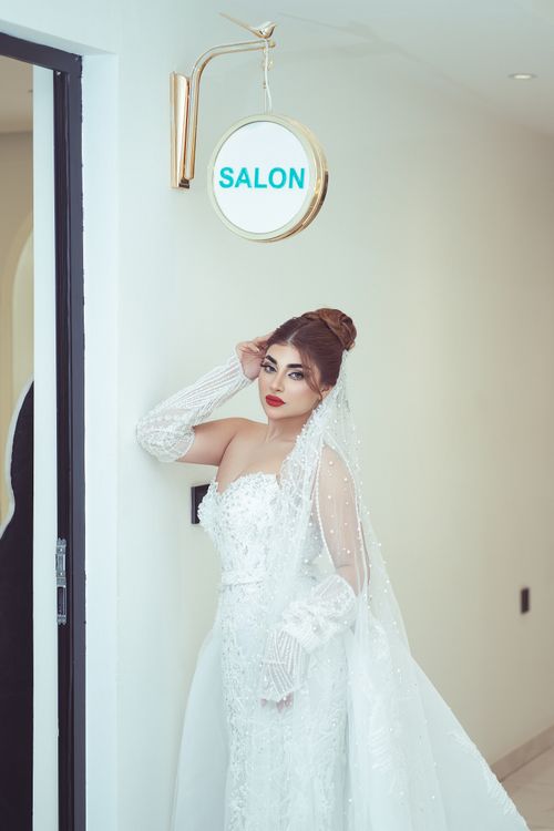 Free A sophisticated bride in a white gown poses gracefully near a salon sign. Stock Photo