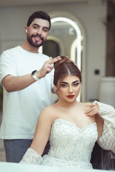 A bride in a white dress gets her hair styled by a professional hairstylist in a salon.