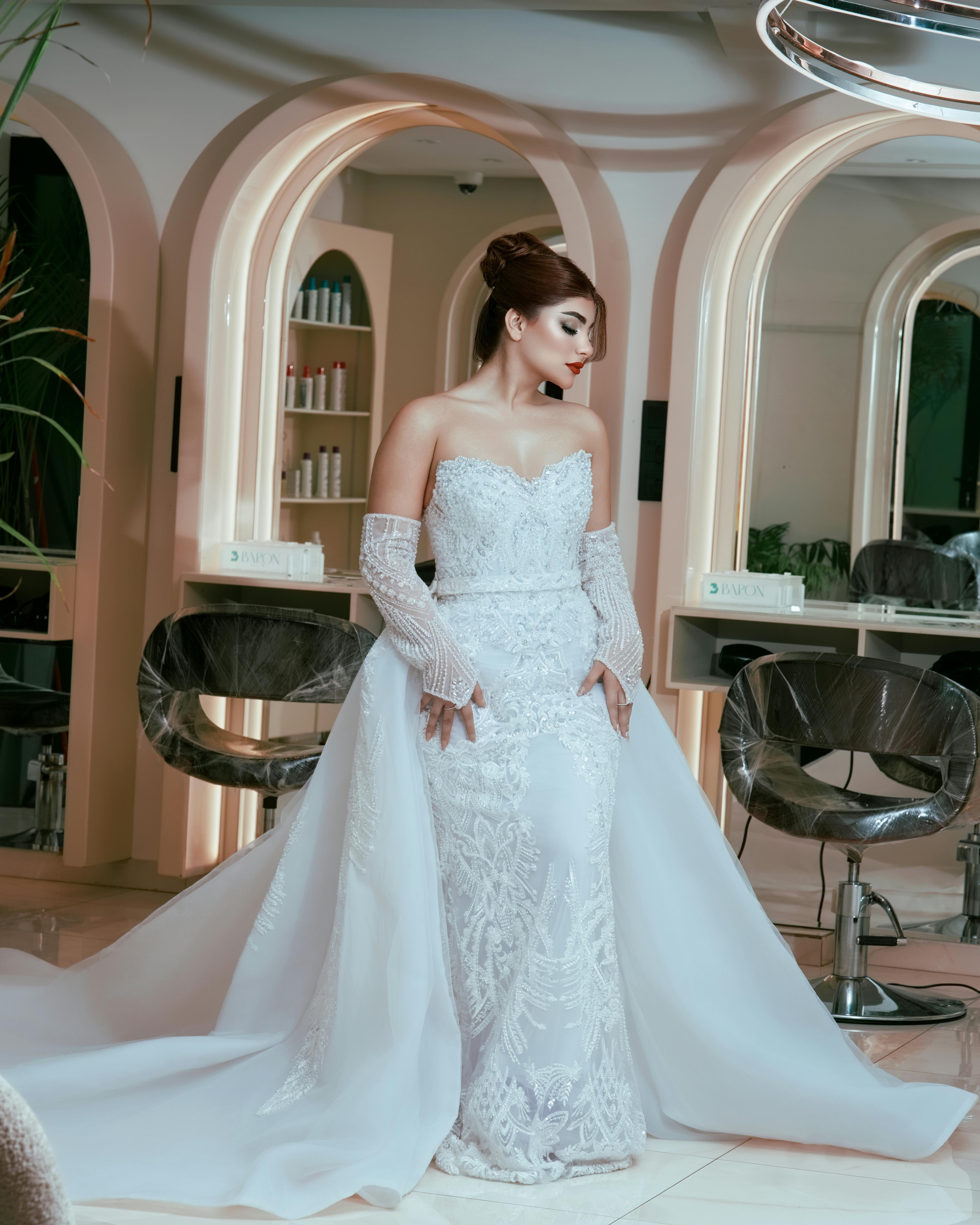 Bride wearing a stunning white wedding gown with elegant lace detailing in a modern salon setting.