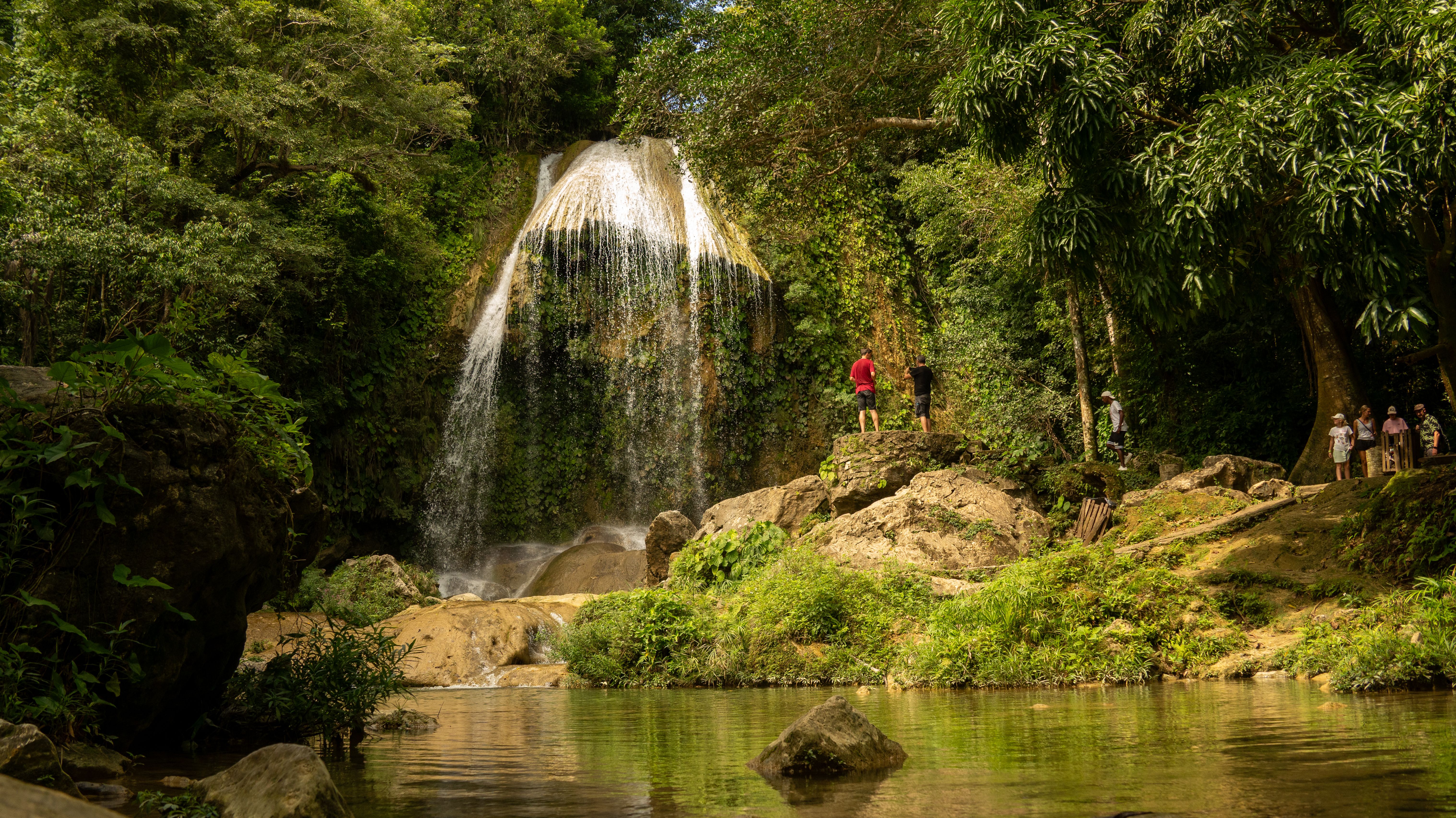 A beautiful waterfall surrounded by lush greenery and rocks with people exploring the area.