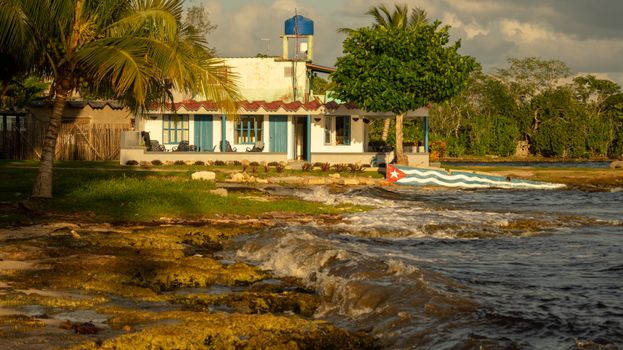 Charming seaside house in Cuba with lush greenery and ocean waves splashing the shore.