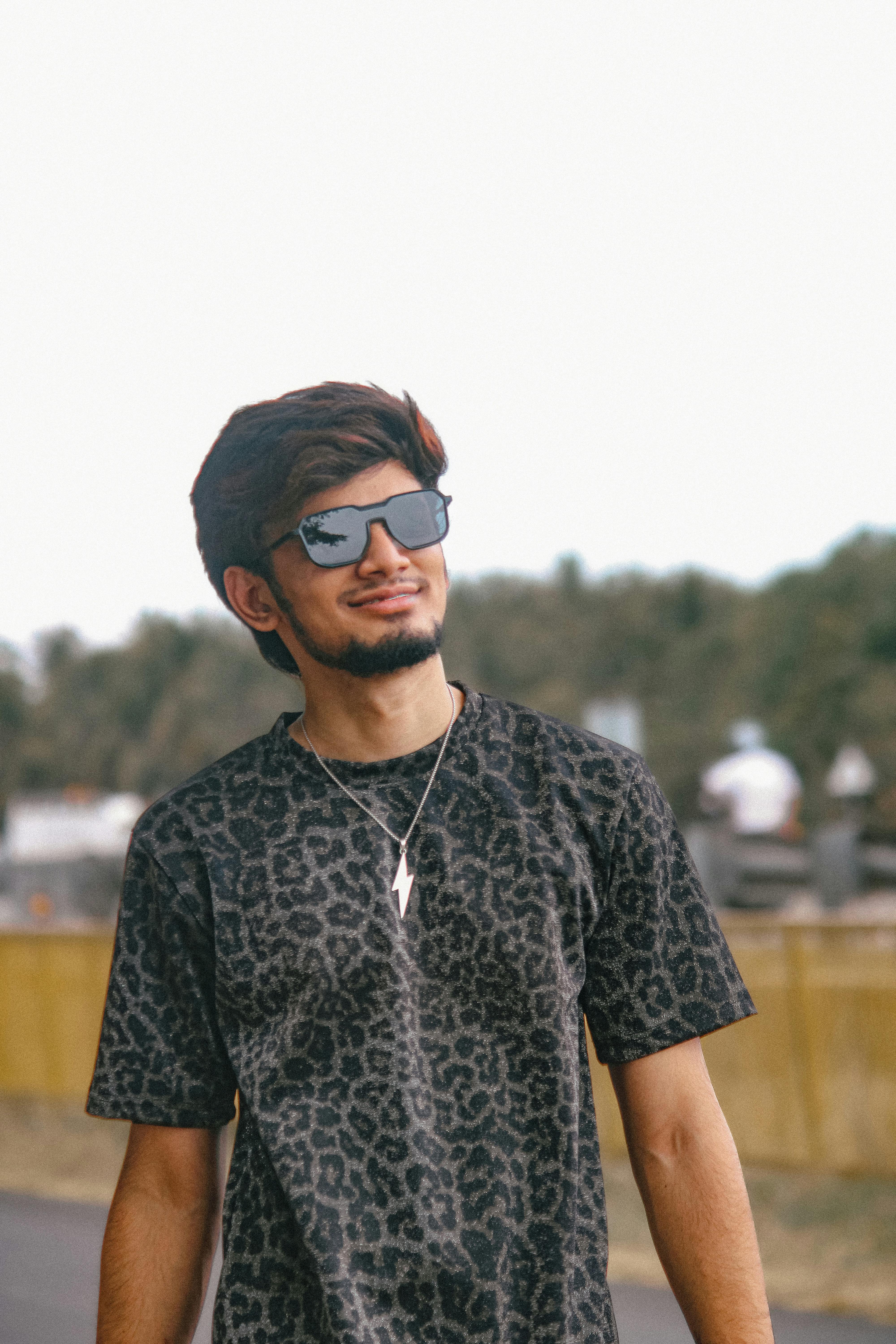 Confident young man wearing sunglasses and stylish shirt outdoors.