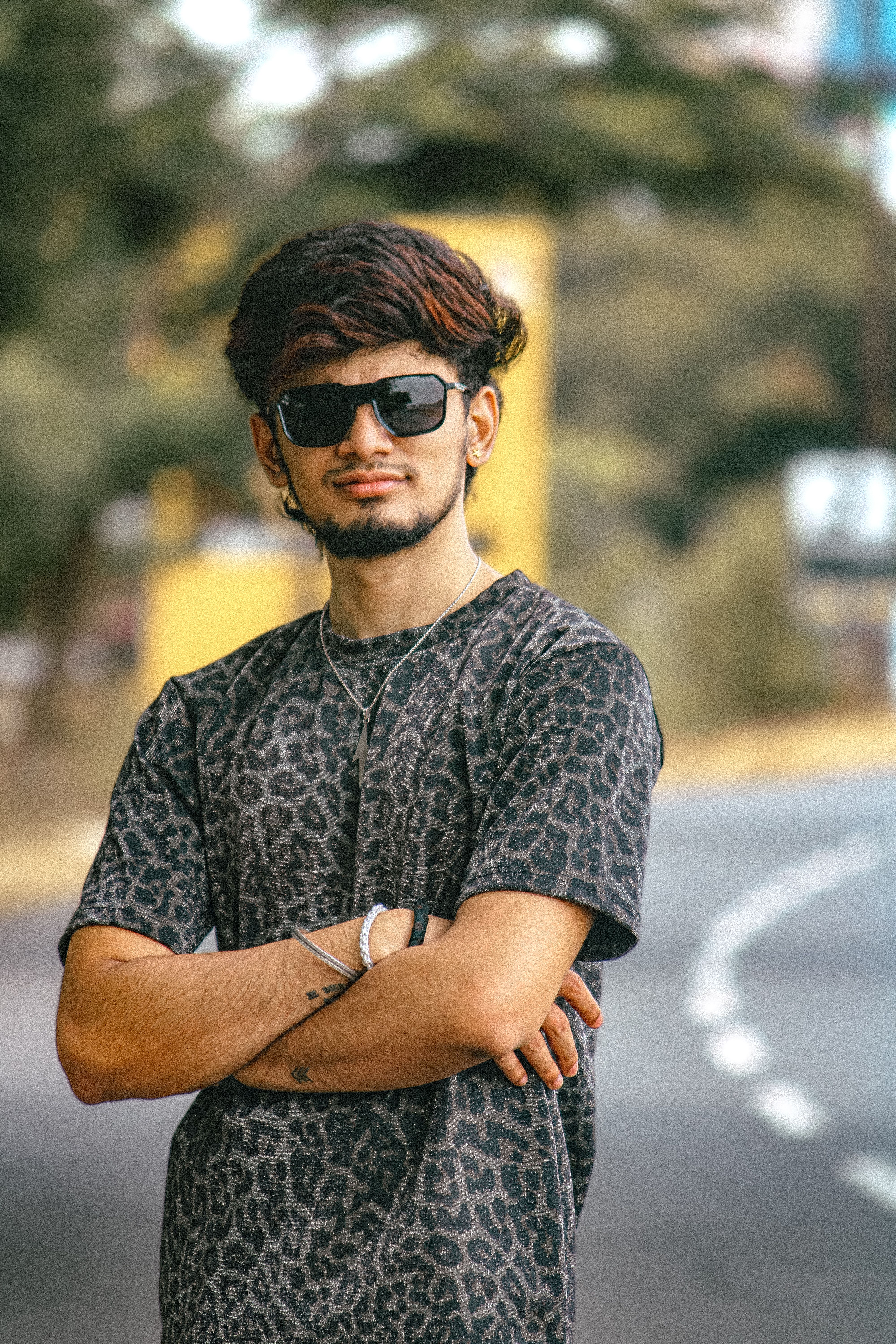 Confident young man wearing sunglasses and leopard print shirt standing on a street.