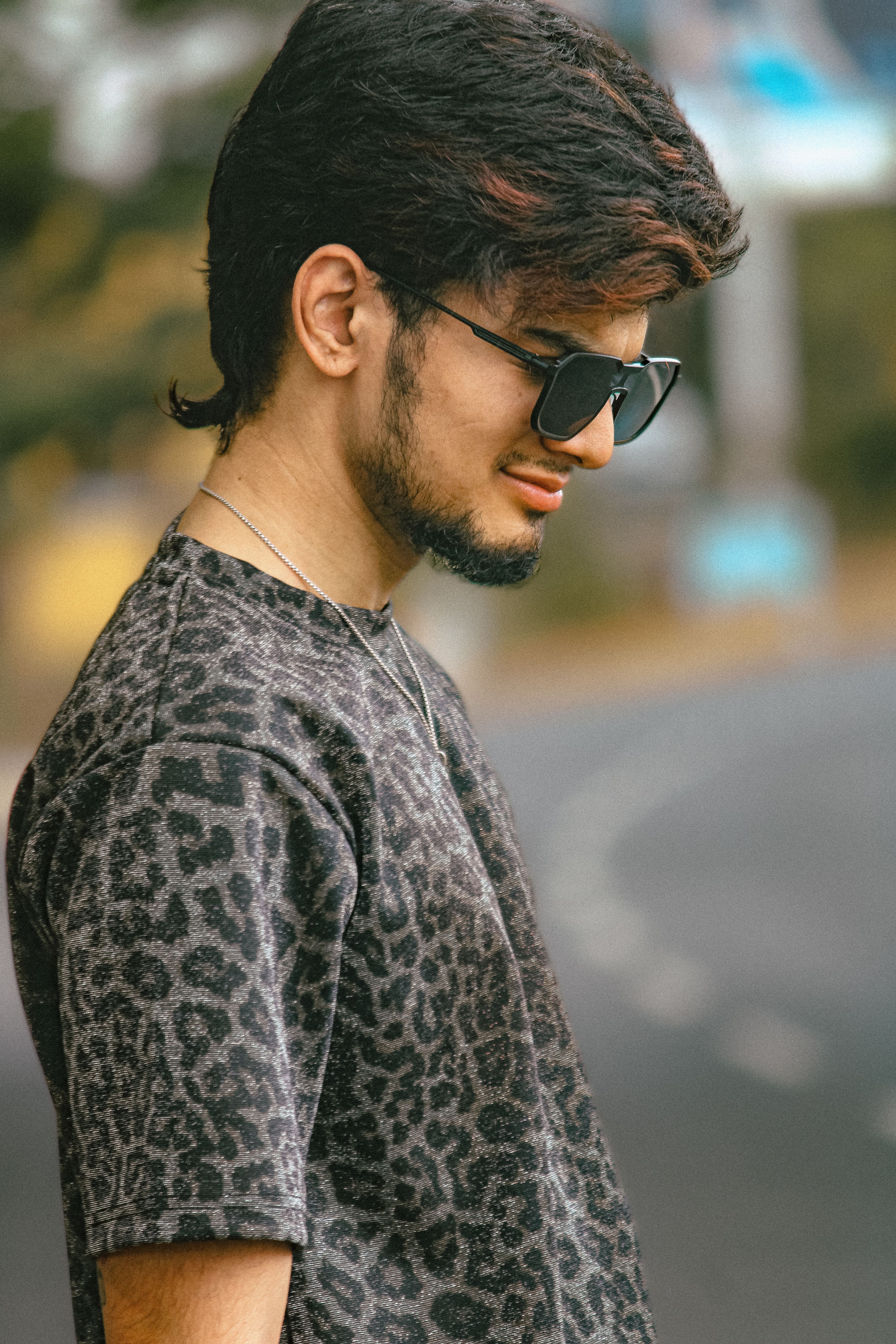 Casual portrait of a young man wearing sunglasses on a blurred outdoor background.