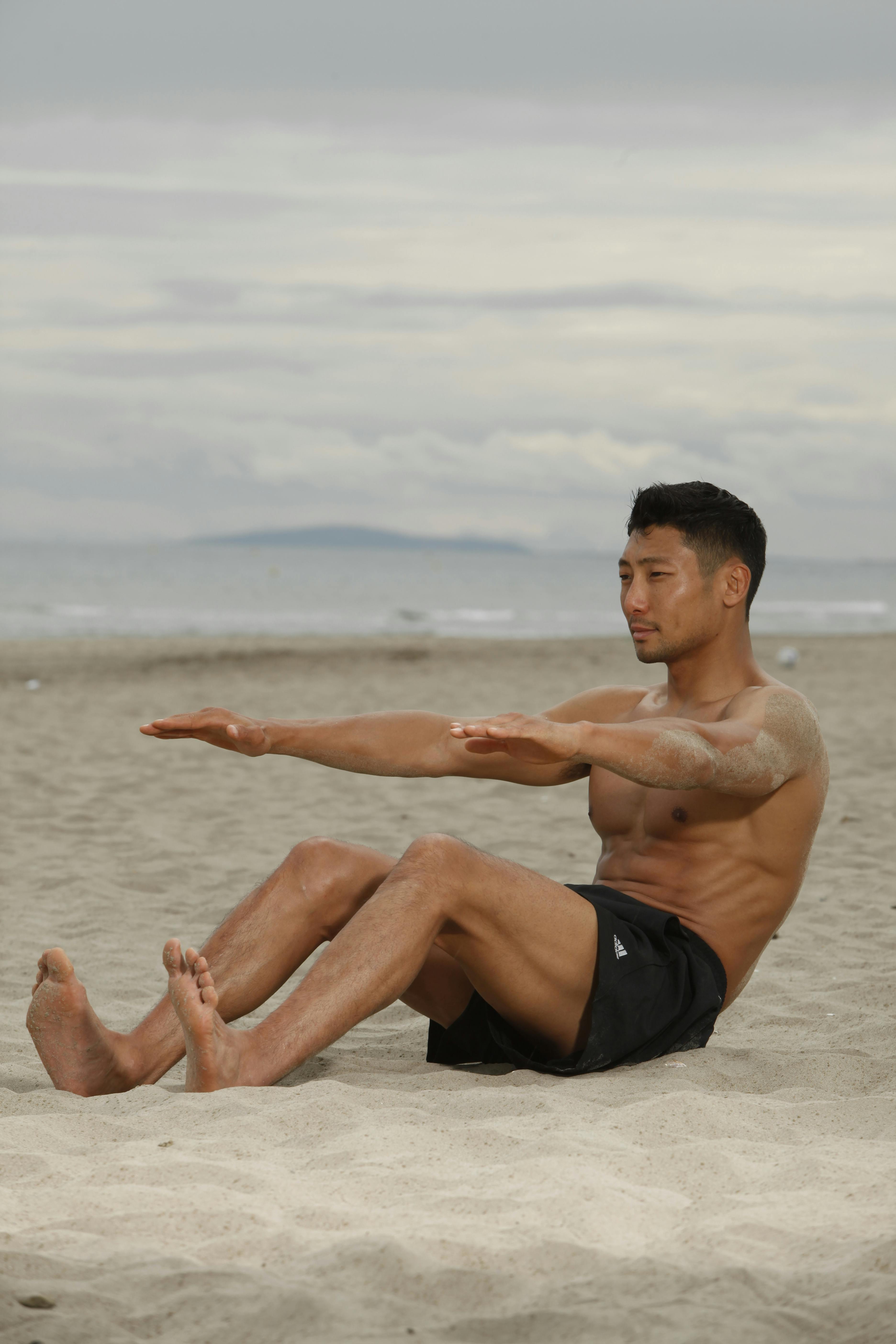 A fit adult male performing a core workout on a sandy beach, displaying strength and focus.