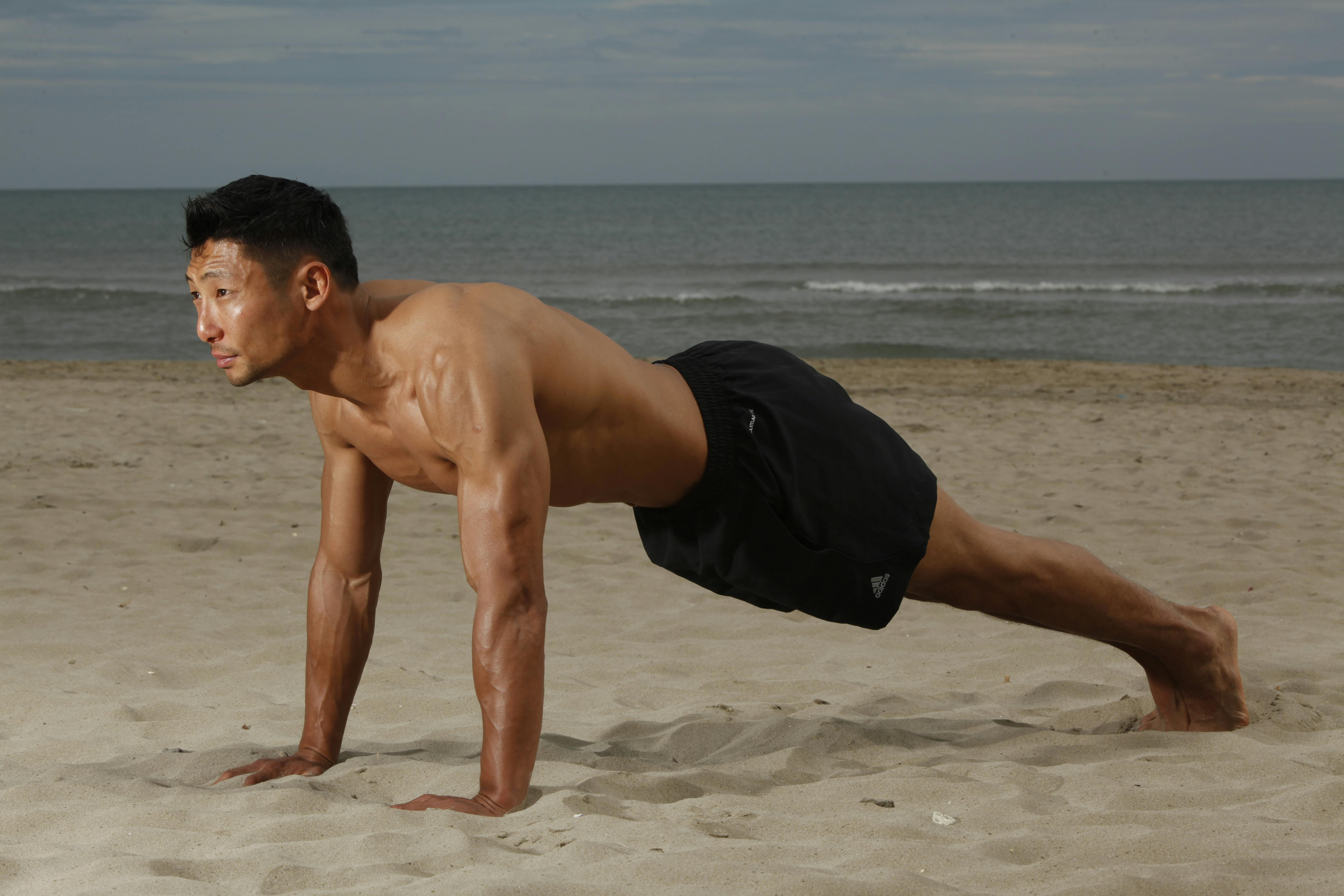Fit man doing a plank exercise on a sunny beach, showcasing strength and fitness.