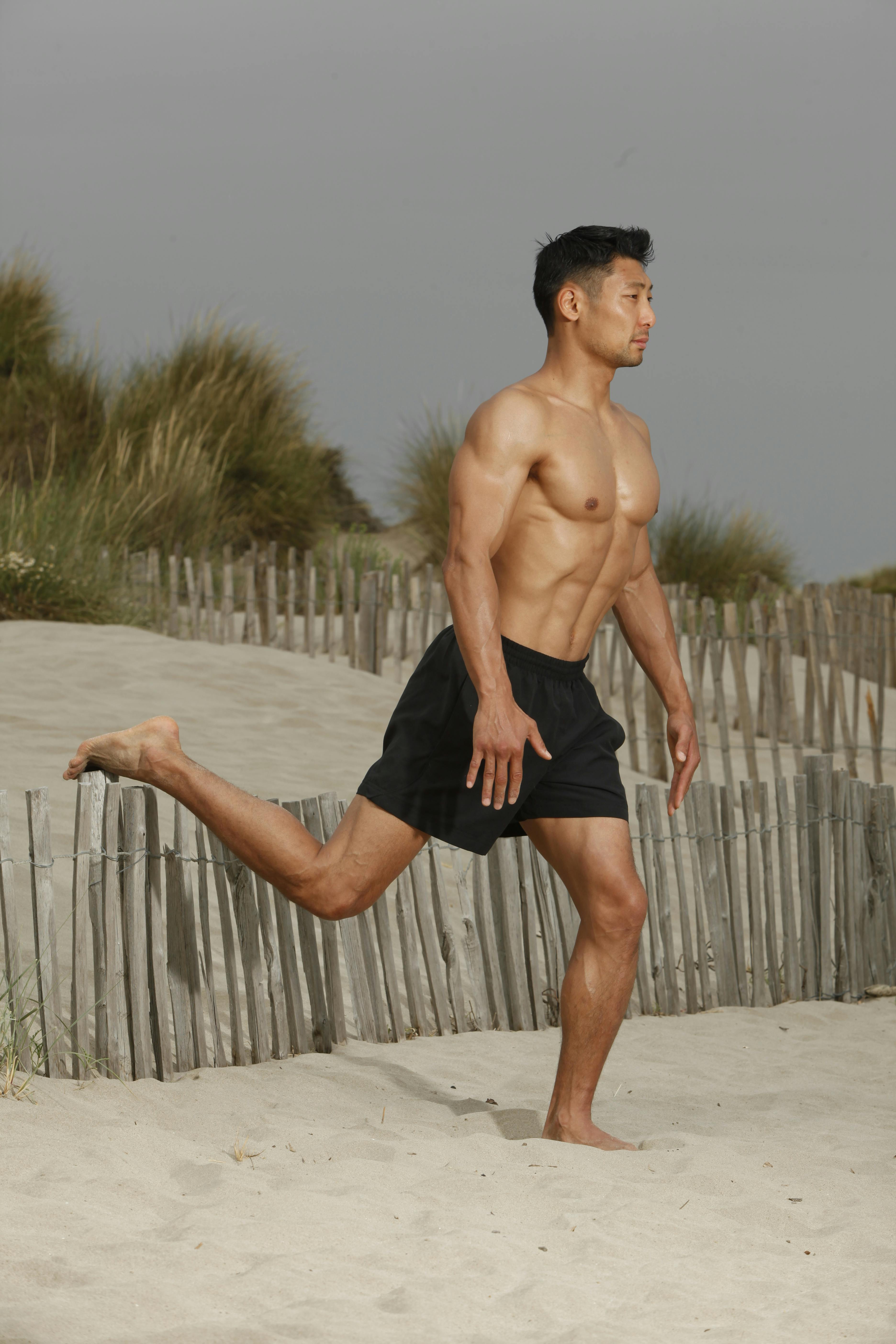 Muscular man performing exercises on a sandy beach outdoors.