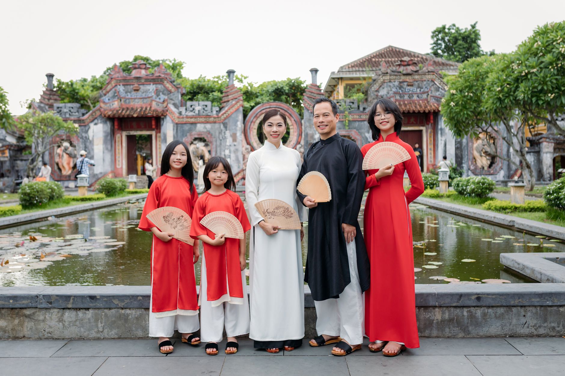 Family wearing traditional Vietnamese clothing at a temple in Hội An, Vietnam, holding fans.