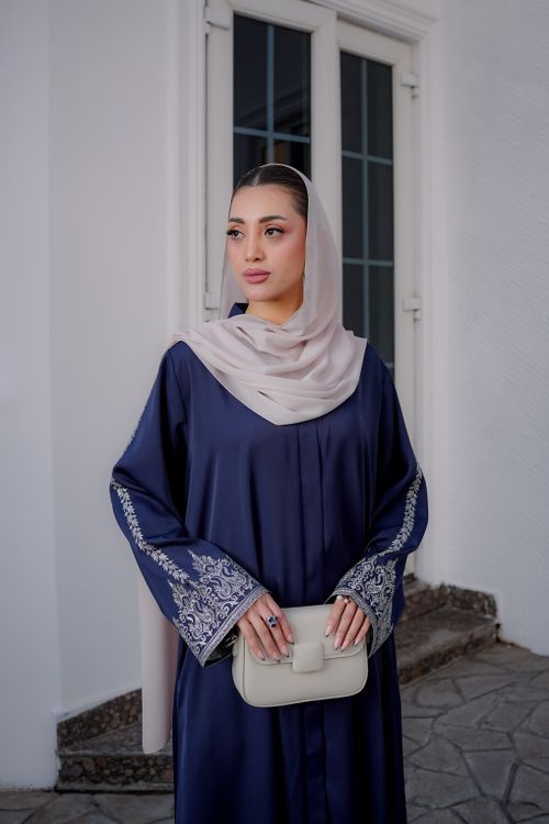 Free A stylish woman in a blue embroidered dress and hijab poses outdoors, showcasing modern modest fashion. Stock Photo