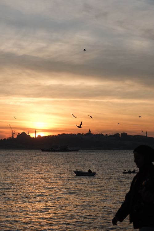 Free A stunning sunset over the ocean in Istanbul, with silhouettes of people and boats. Stock Photo