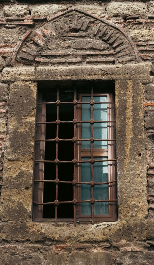 Free Rustic stone wall with a barred window showcasing ancient architectural style. Stock Photo