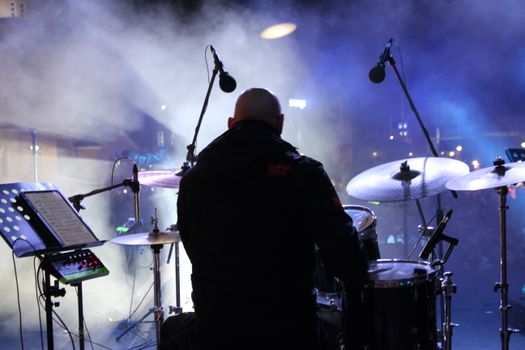 A drummer performing live at a concert with stage lights and smoke effects enhancing the ambiance.