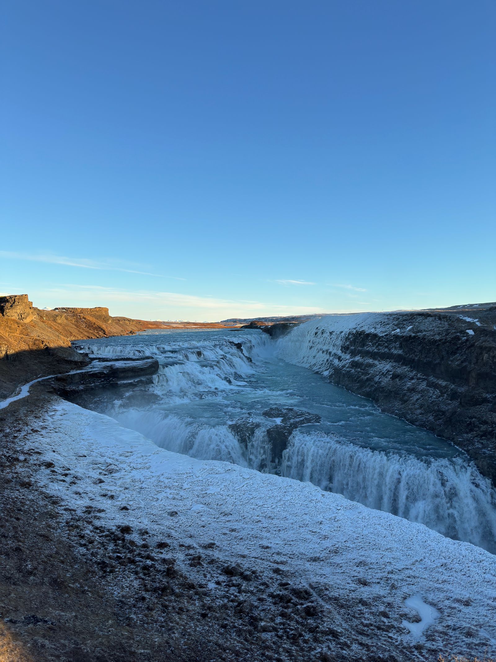 Gullfoss waterfall tumbling into a deep, icy canyon under a bright blue sky