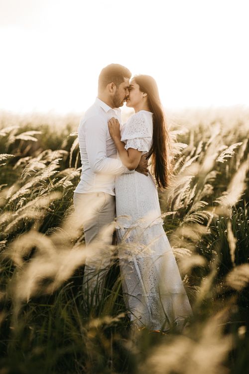 Free A loving couple in a white dress and shirt embracing in a sunlit field. Stock Photo