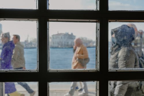 Free Blurry pedestrians through a glass window with a waterfront backdrop, creating a dynamic cityscape. Stock Photo
