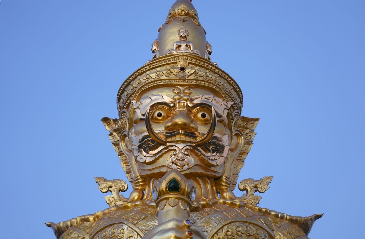 close up of a golden guardian statue at wat phra that doi kham chiang