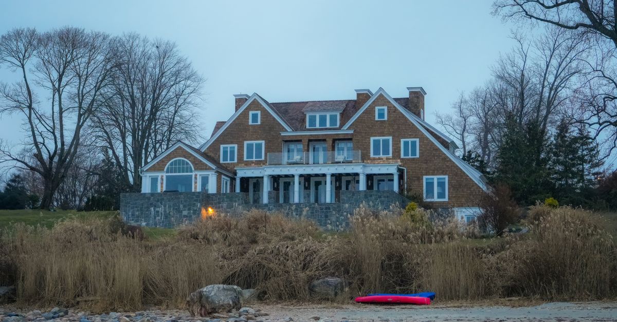Beautiful lakefront house with rustic design surrounded by bare trees in winter.