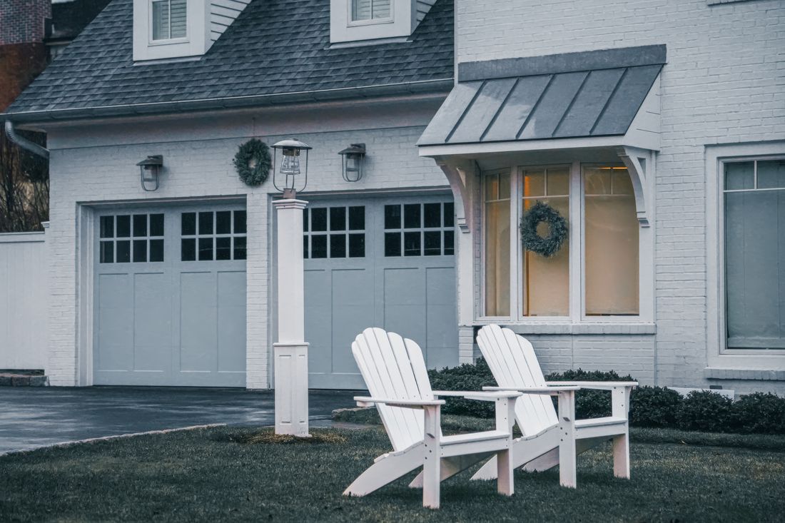 Two white Adirondack chairs in front of a cozy suburban home
