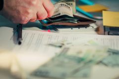 Close-up of hands counting cash next to a wallet and documents on a desk.