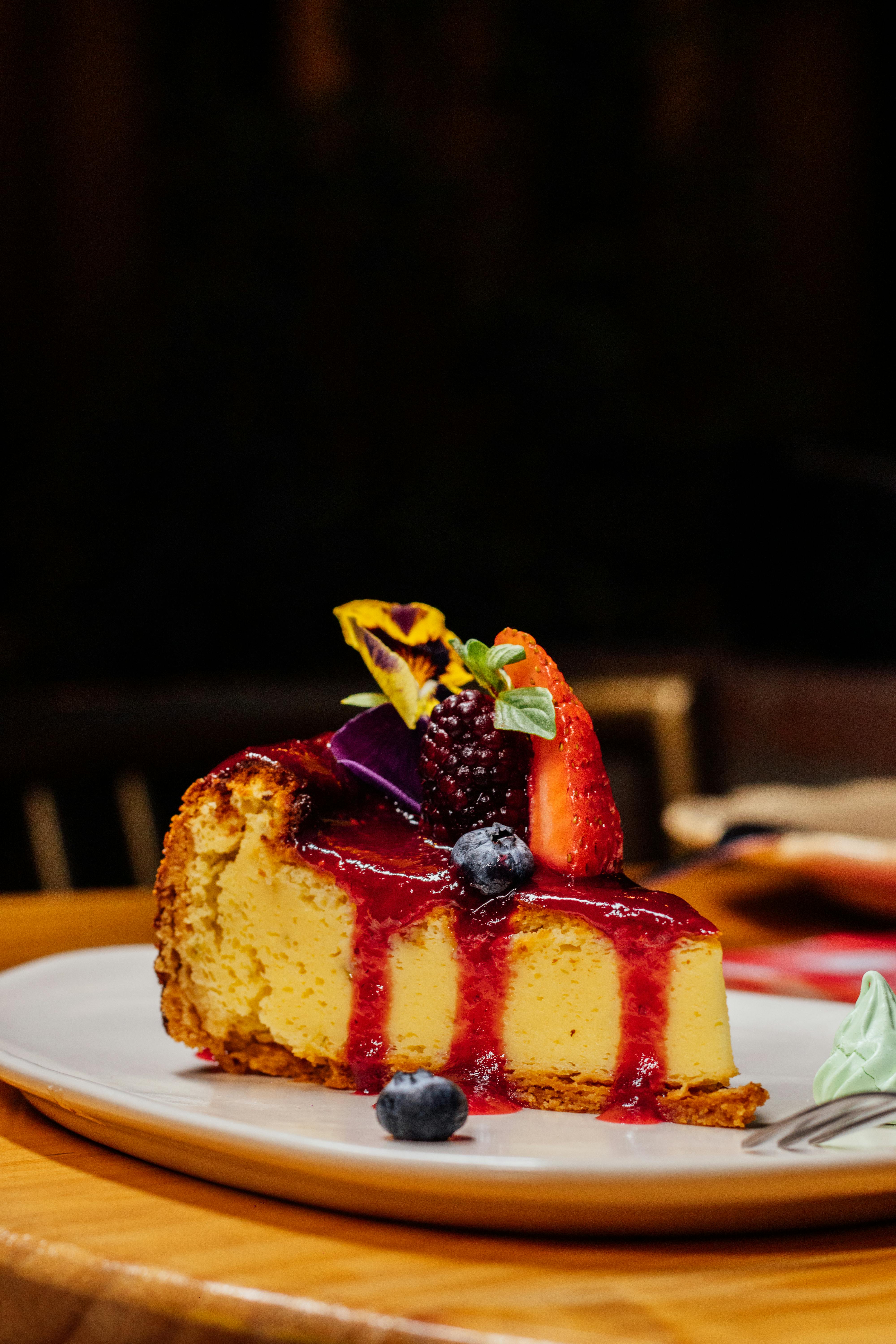 Slice of cheesecake topped with fresh berries and drizzled sauce, served on a plate.