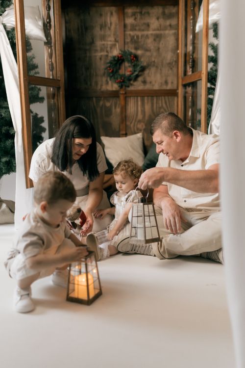 Free A family with young children sharing a warm moment indoors, holding lanterns in a cozy winter setting. Stock Photo