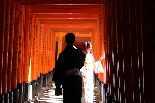 Free Back view of Japanese man and woman in traditional kimonos walking in red Torri gates of Fushimi Inari taisha shrine Stock Photo