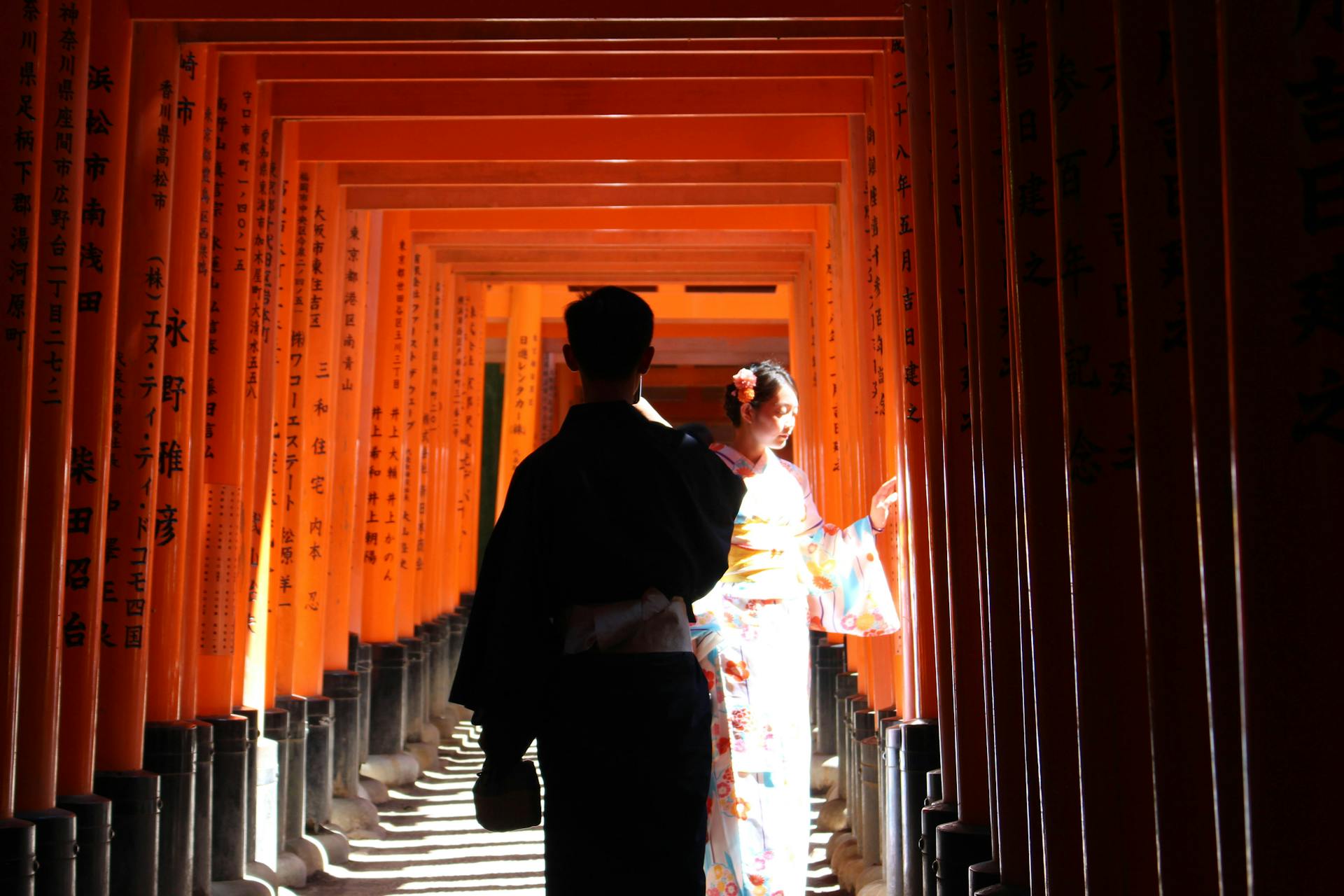 Back view of Japanese man and woman in traditional kimonos walking in red Torri gates of Fushimi Inari taisha shrine