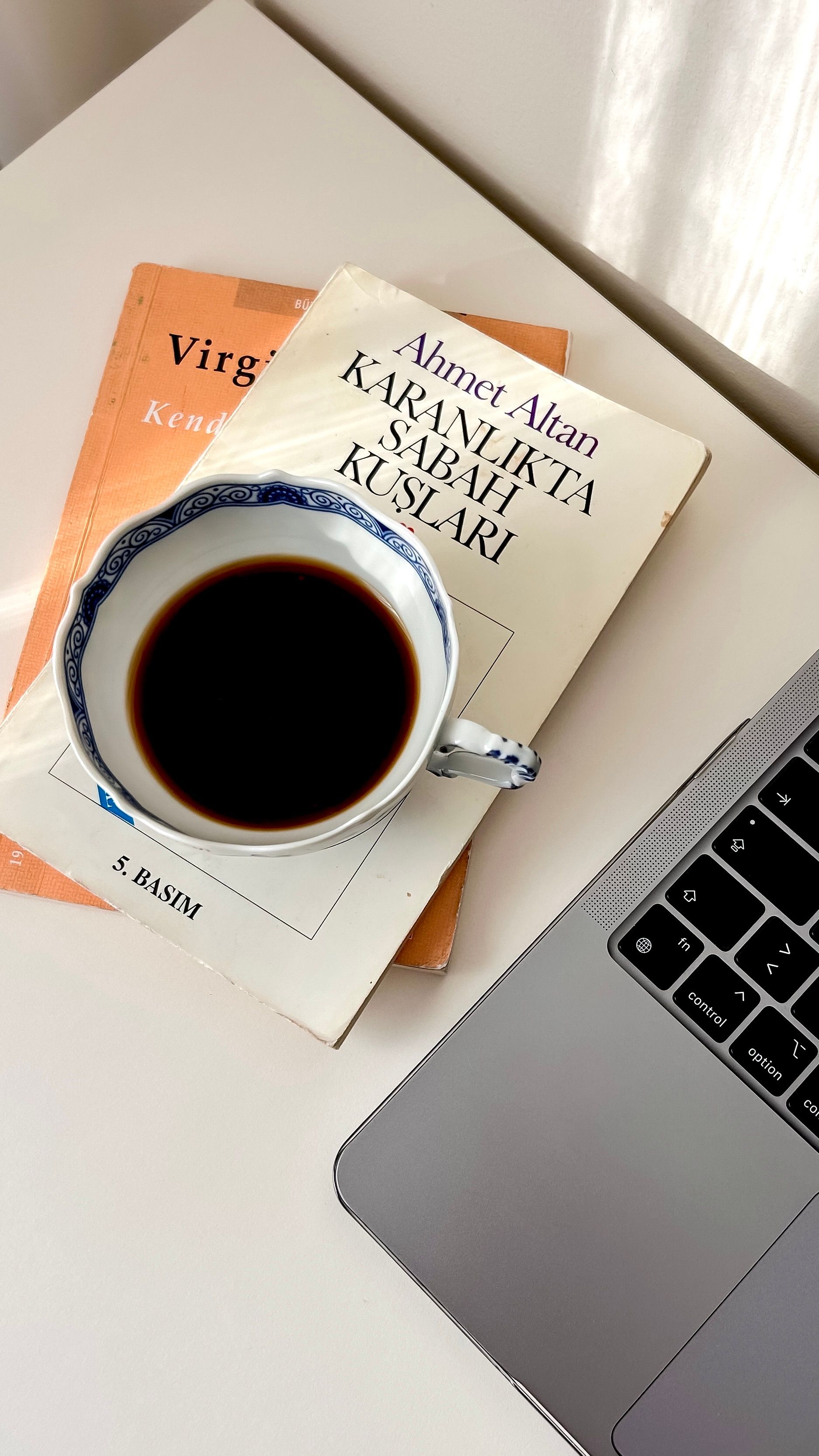 A cup of coffee on a desk with books and a laptop, ideal for work inspiration.