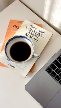 A cup of coffee on a desk with books and a laptop, ideal for work inspiration.
