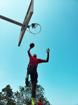 Dynamic shot of a basketball player jumping towards the hoop on a sunny day with clear blue skies.