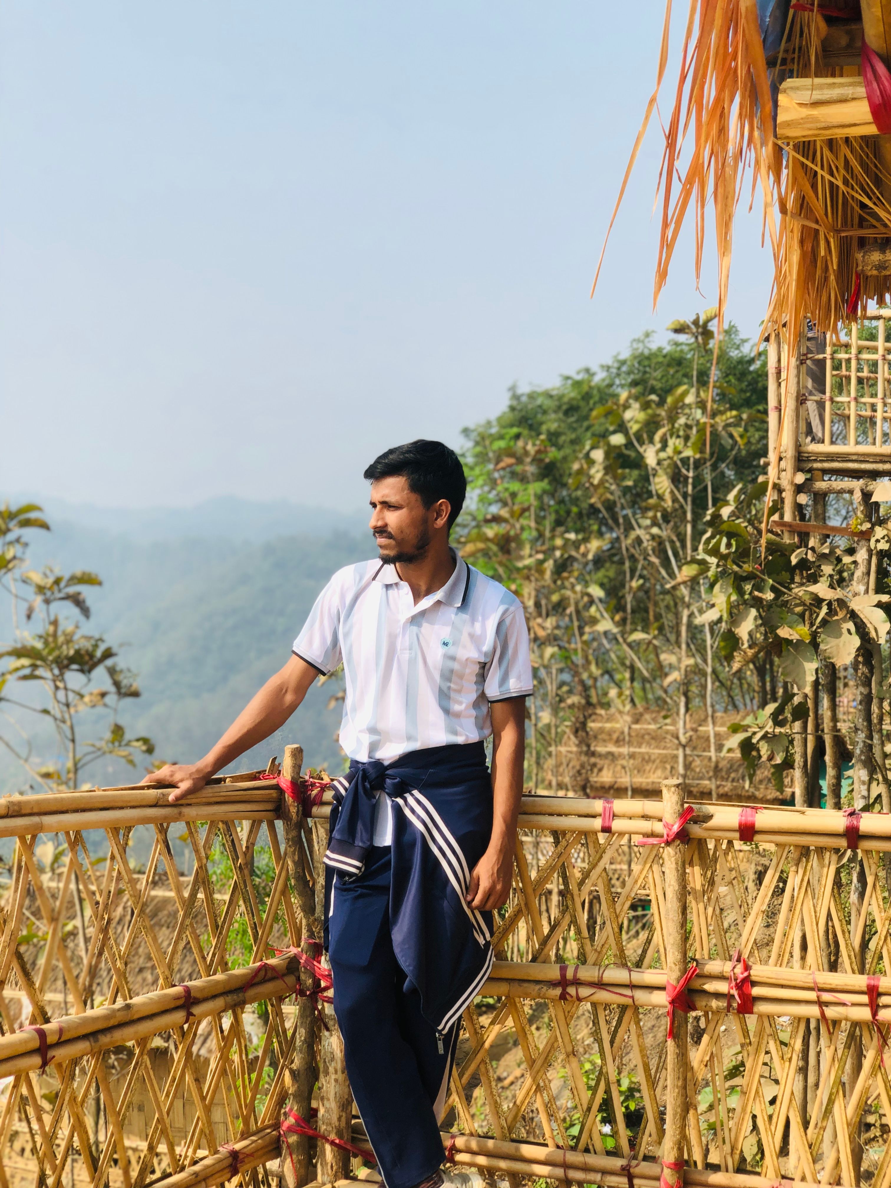 Man gazing at scenic view from a bamboo balcony surrounded by lush greenery.
