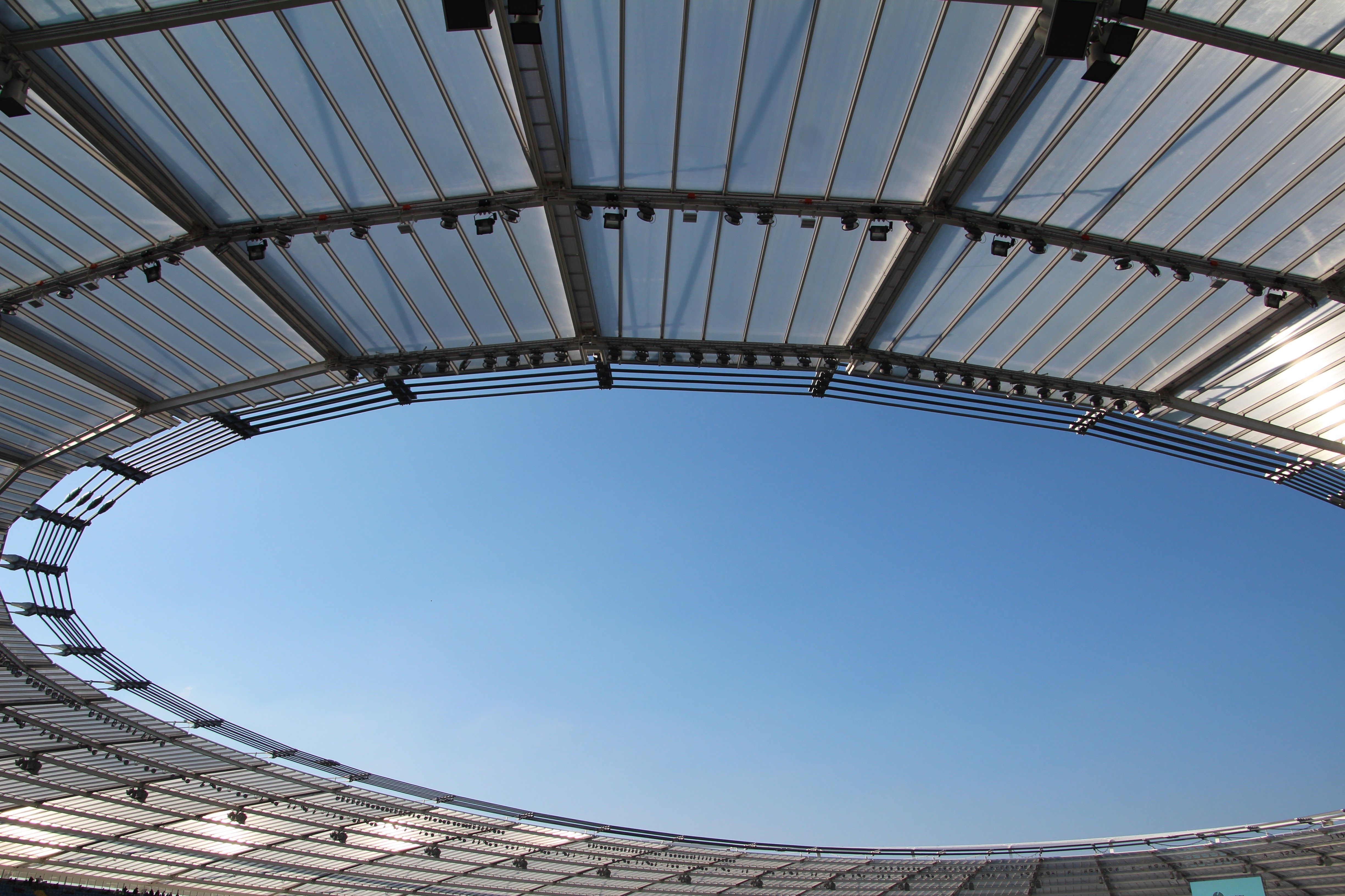 A modern stadium roof design framing a clear blue sky, illustrating structural elegance and openness.