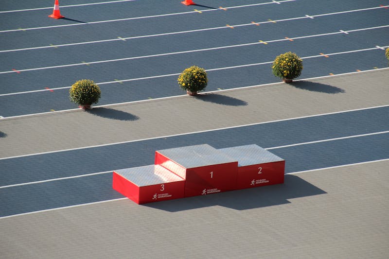 Red podium on a sunny outdoor athletics track with decorative plants.