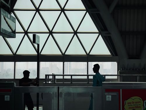 Free Silhouette view of people in an urban transit station with geometric windows and cityscape in the background. Stock Photo