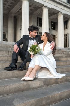 Bride and groom in formal attire sharing a moment on grand steps outdoors.