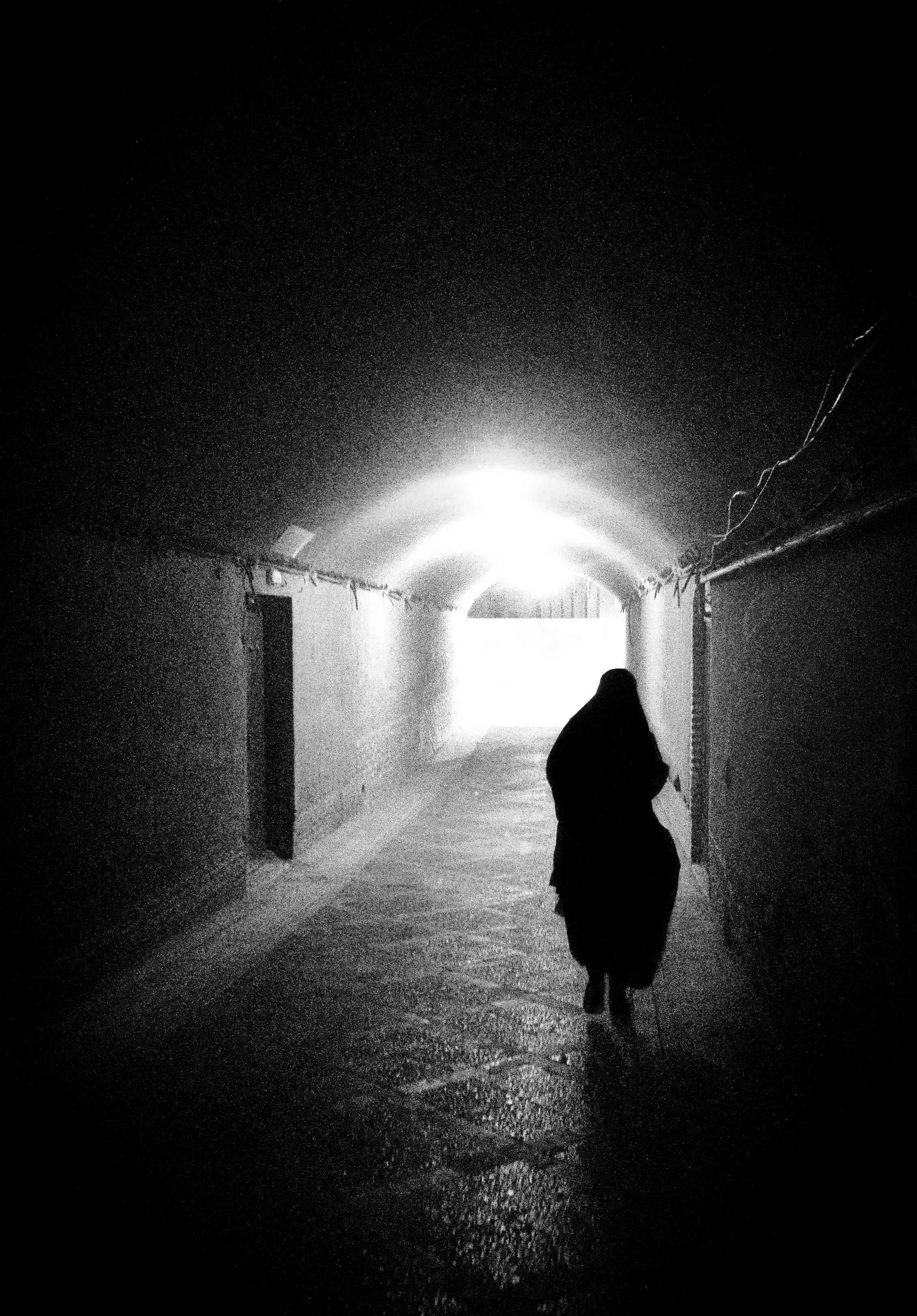 Gratis Una sagoma misteriosa cammina in un vicolo scarsamente illuminato di Yezd, evidenziando il gioco di luci e ombre. Foto a disposizione